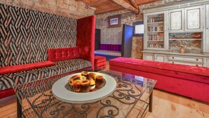 Una sala de estar acogedora con un papel tapiz estampado, un sofá rojo, una mesa de centro de vidrio con fruta y una estantería.