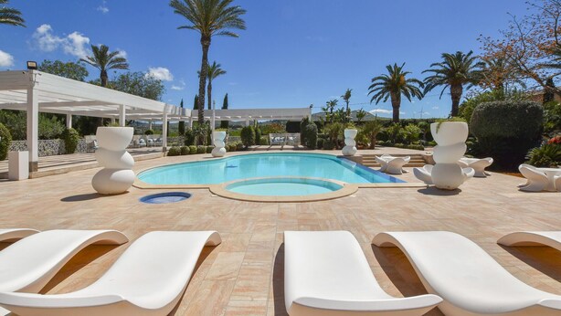 Un área junto a la piscina con modernas sillas de descanso, un espacio de estar cubierto y una piscina azul cristalina.