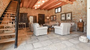 Una habitación con paredes de piedra, una escalera, dos sofás, una mesa de centro y un armario de madera.