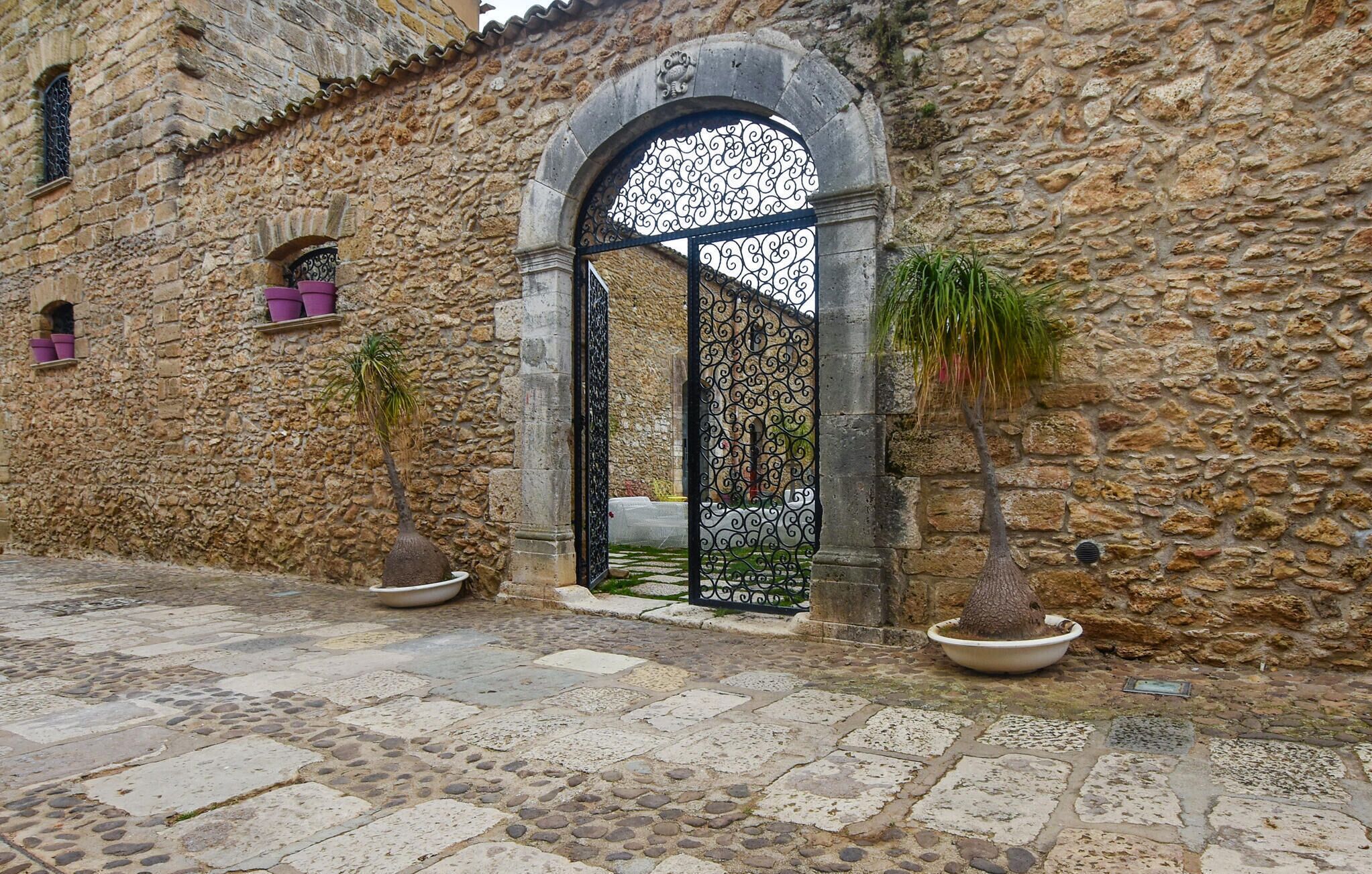 Un bâtiment en pierre doté d’une grande entrée en arc de cercle, de plantes en pot et d’une cour pavée.