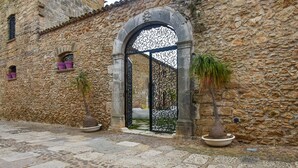 Un edificio de piedra con un gran arco de entrada, plantas en macetas y un patio adoquinado.