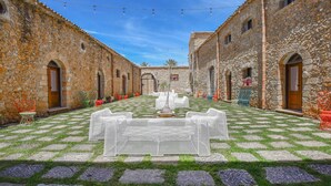 Un patio con edificios de piedra, una mesa central y luces colgantes.