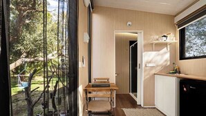 A modern kitchen with a wooden table and chairs, a built-in oven, and a large window overlooking a garden. - Metung Hideaway by Tiny Away (Metung)