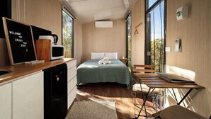 A compact room with a bed, a small table, a chair, a microwave, a coffee maker, and a sign. - Metung Hideaway by Tiny Away (Metung)