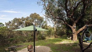 A wooden deck with a green umbrella, a rustic table, and a hanging hammock. - Metung Hideaway by Tiny Away (Metung)