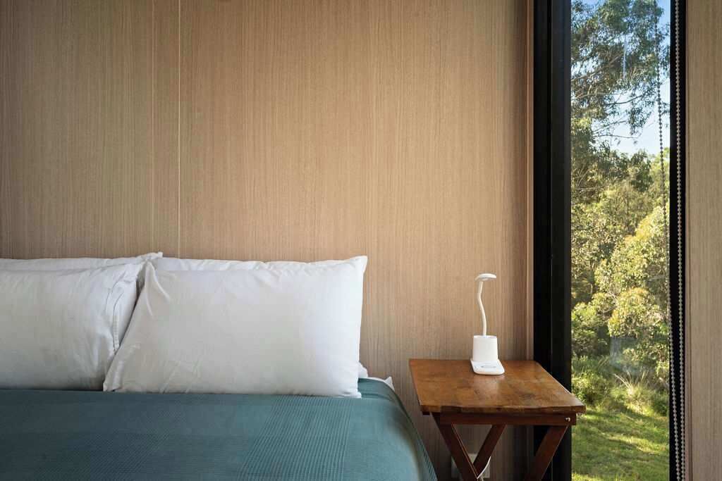 A bedroom with a bed, a nightstand, and a window with a view of trees.