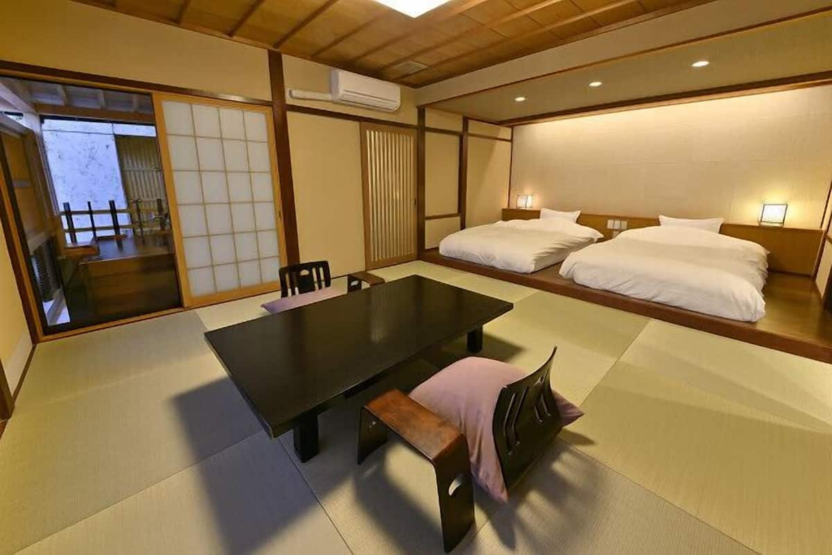 A traditional Japanese room with tatami flooring, a low table, two beds, sliding doors, and a view of a garden.