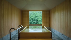 Interior de madera con una bañera de vidrio y vistas a árboles verdes a través de una ventana.