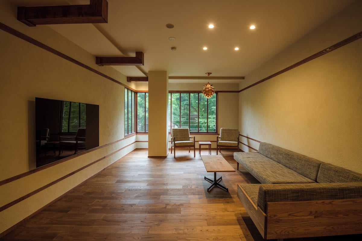 A spacious room with wooden flooring, a large window, and a seating area with a sofa and chairs.