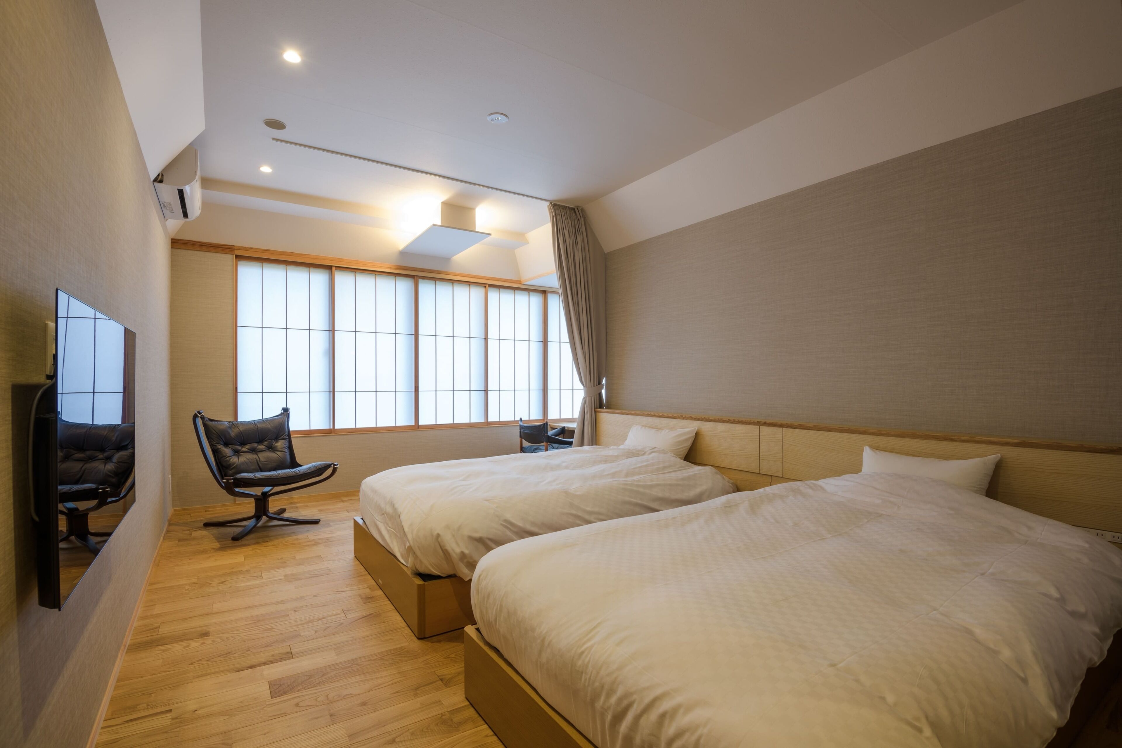 A hotel room with two beds, a chair, a TV, and a large window.
