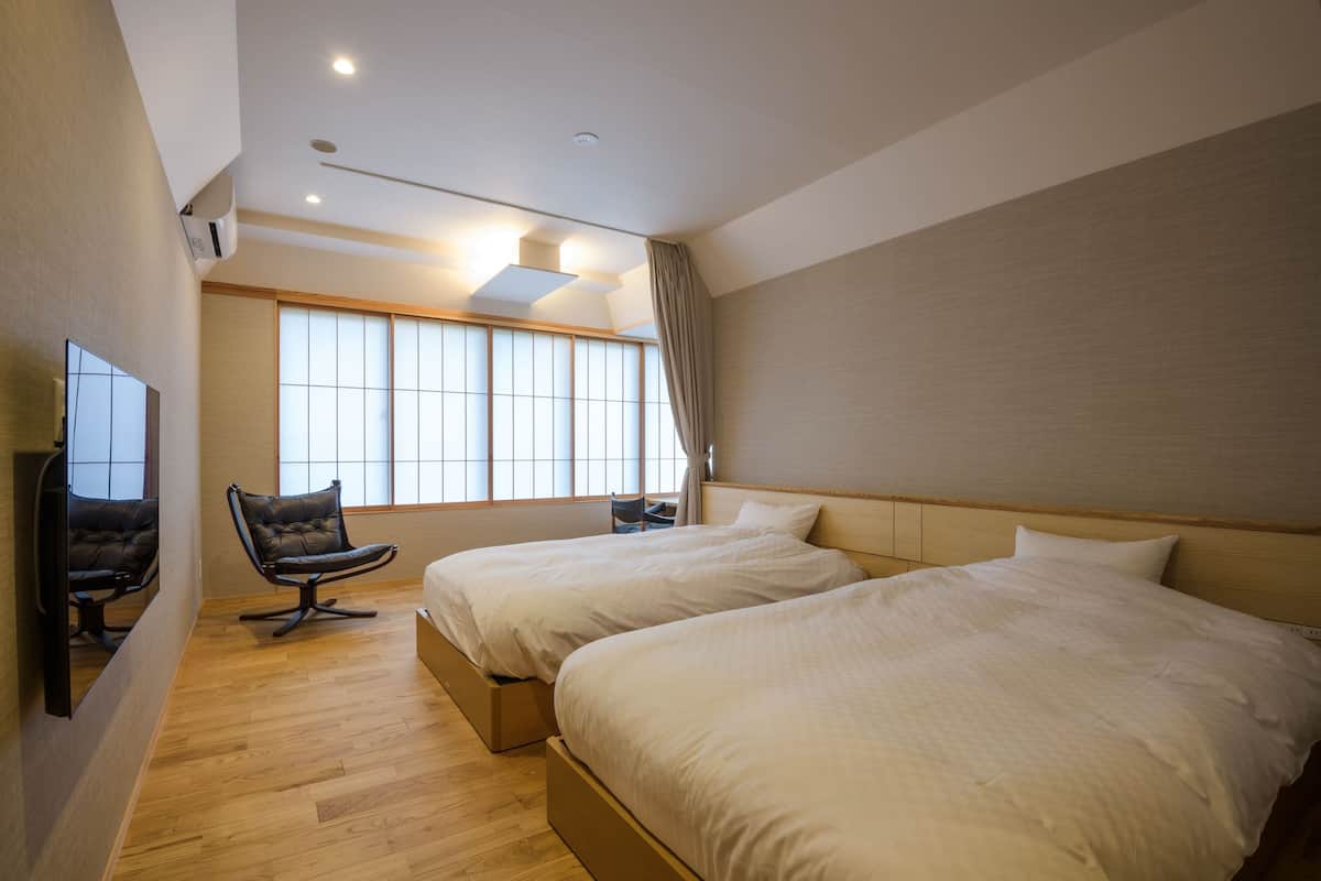 A hotel room with two beds, a chair, a TV, and a large window.