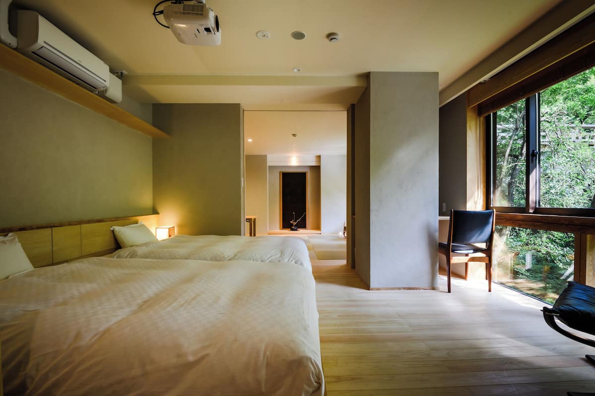 A hotel room with two beds, a large window, and a view of the outdoors.