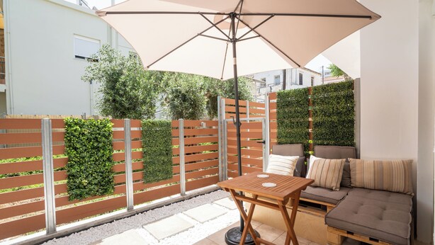 A patio with a wooden table and a cushioned seating area under a large umbrella. - Warm and colourfull  studio in historical district of Chania (Chania)