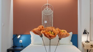 A bedroom with a bed, a bedside table with a lamp, a decorative hanging, and a vase with flowers. - Warm and colourfull  studio in historical district of Chania (Chania)