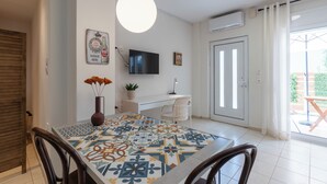 A dining area with a tiled table, chairs, a vase with flowers, a television on the wall, and a sliding glass door leading to an outdoor area. - Warm and colourfull  studio in historical district of Chania (Chania)