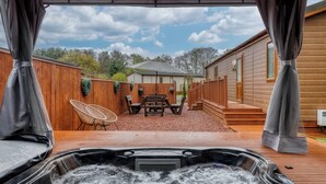 Un jacuzzi con terraza de madera y un patio cubierto con mesa y sillas.