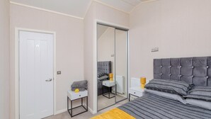 Un dormitorio con una cama, mesita de noche, espejo, armario y puerta.