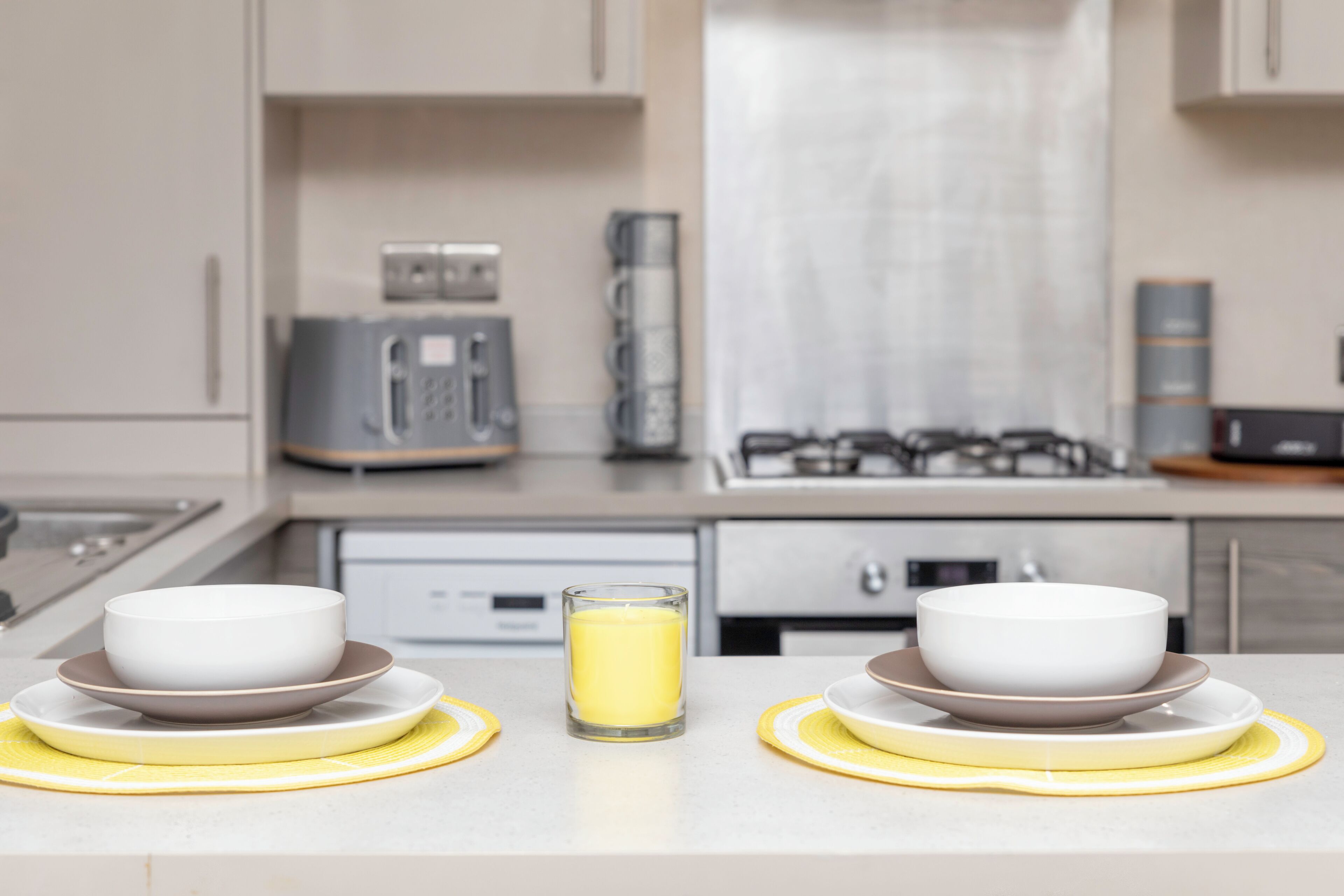 Uma cozinha moderna com duas tigelas em jogos americanos amarelos, um copo de líquido amarelo e uma cafeteira.
