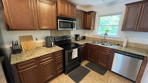 A kitchen with wooden cabinets, a microwave, stove, and dishwasher. - Spacious Cottage in Rogers. Central: bike trails, restaurants, work, everything! (Rogers)