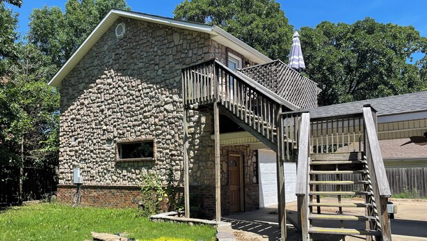 A stone house with a wooden staircase leading to a porch. - Spacious Cottage in Rogers. Central: bike trails, restaurants, work, everything! (Rogers)
