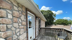 A stone building with a white door, a wooden deck, and outdoor seating. - Spacious Cottage in Rogers. Central: bike trails, restaurants, work, everything! (Rogers)
