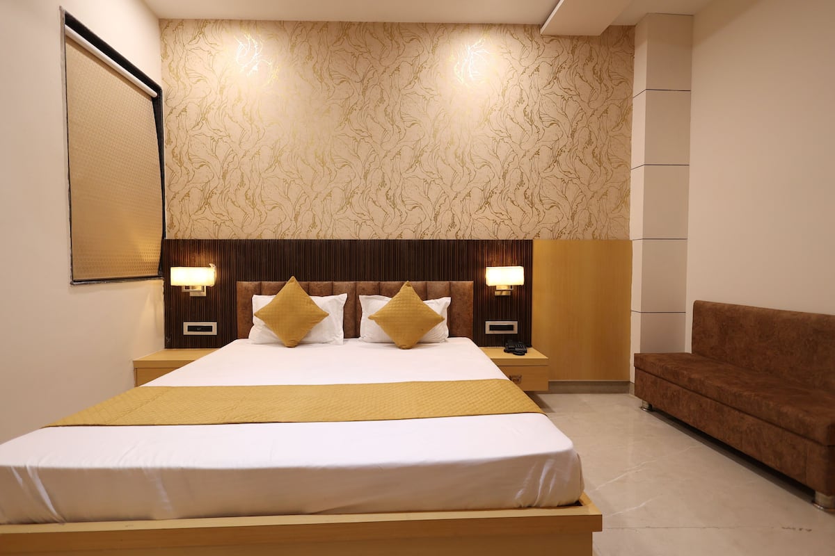 A hotel room with a large bed, two bedside tables with lamps, a brown sofa, and a patterned wallpaper.