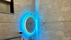 A modern bathroom with a white sink, a mirror, and a blue illuminated light fixture. - SHRI HARIDAS KUNJ (Mathura)