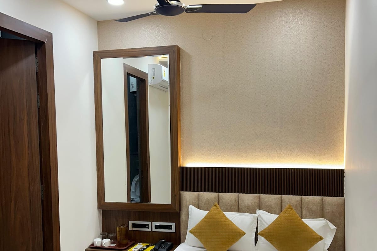 A hotel room with a bed, a ceiling fan, a large mirror, a bedside table with a phone, and a bedside lamp.