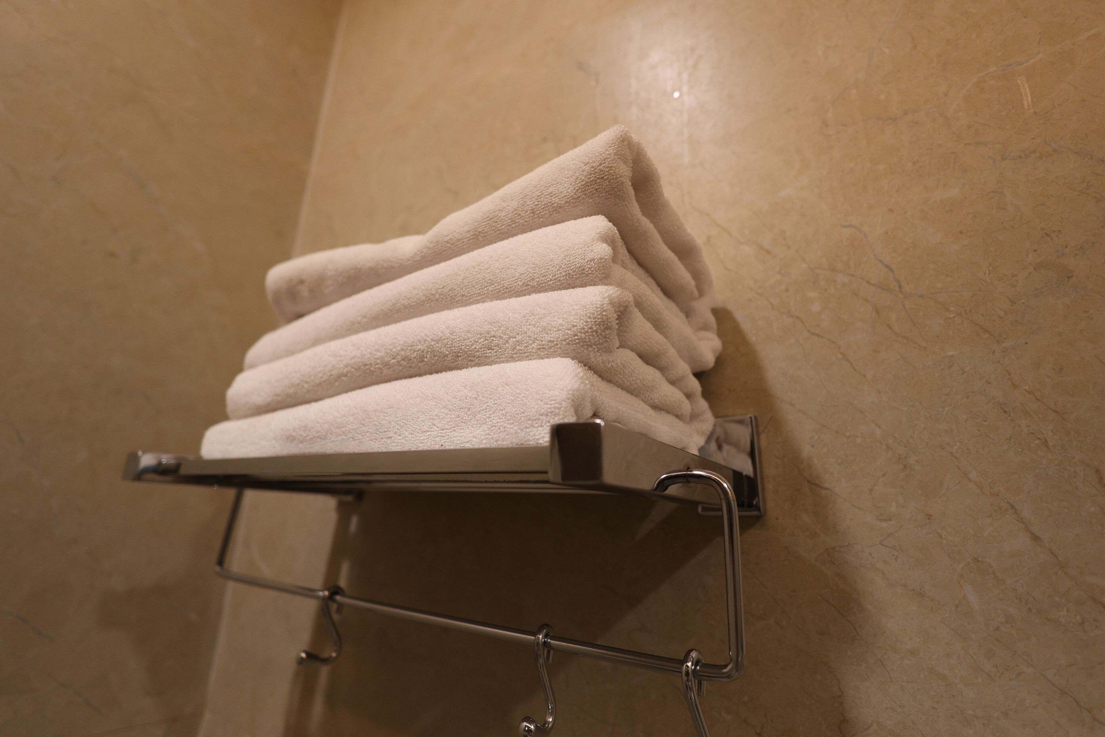 A stack of white towels on a metal towel rack in a bathroom with a beige tiled wall.