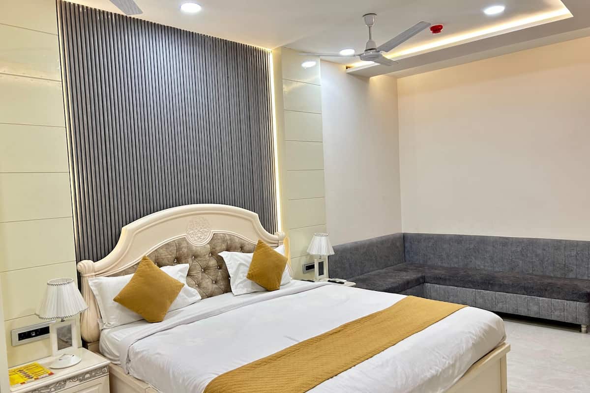 A modern bedroom with a large bed, bedside tables, a nightstand, a lamp, a ceiling fan, and a grey sofa.