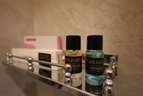 Une étagère de salle de bain avec deux bouteilles de shampoing et d’après-shampoing de la marque Swami Harida, et une boîte de produits roses.