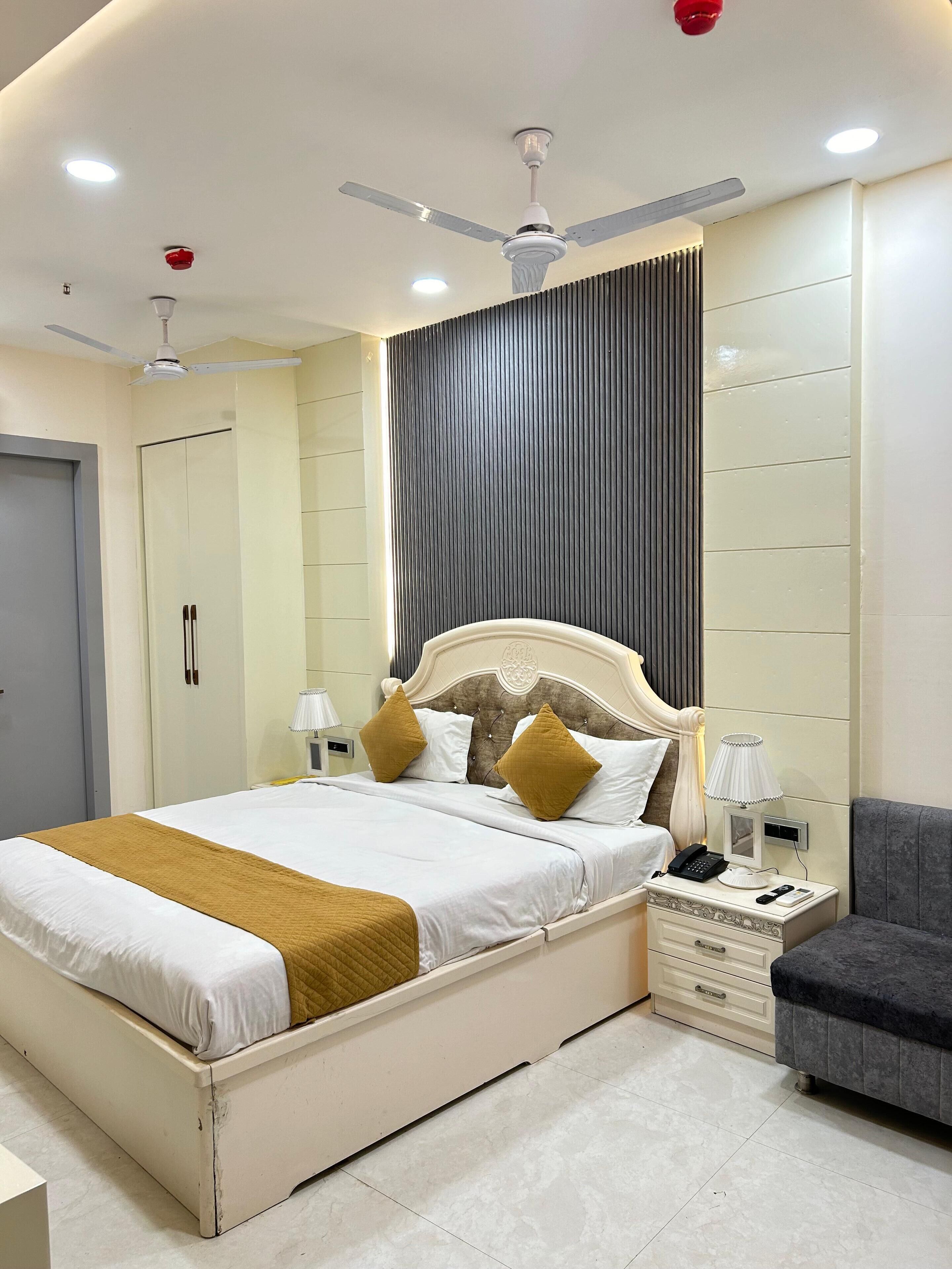 A modern bedroom with a large bed, bedside tables, a nightstand, a grey sofa, and a ceiling fan.