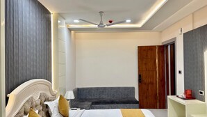 A modern bedroom with a bed, a grey sofa, a wooden wardrobe, and a white bedside table. - SHRI HARIDAS KUNJ (Mathura)