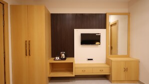 A room with a wooden wardrobe, a TV on a wall, a mirror, and a small table with a coffee pot. - SHRI HARIDAS KUNJ (Mathura)