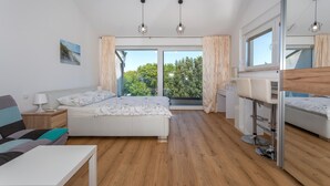 A modern bedroom with a bed, bedside table, lamp, and a view of trees through large windows.