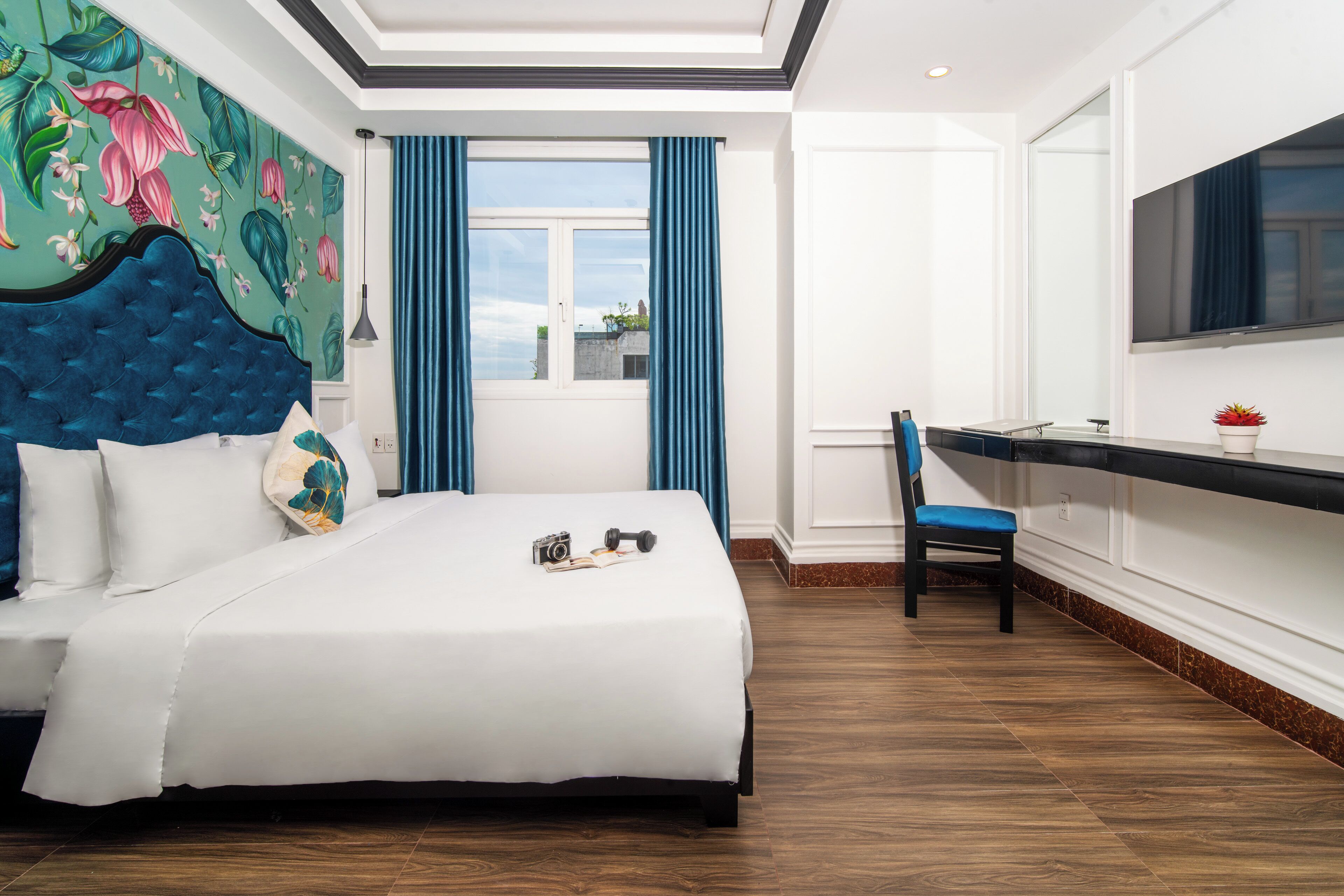A hotel room with a large bed, a desk with a chair, a TV, and a window with curtains.
