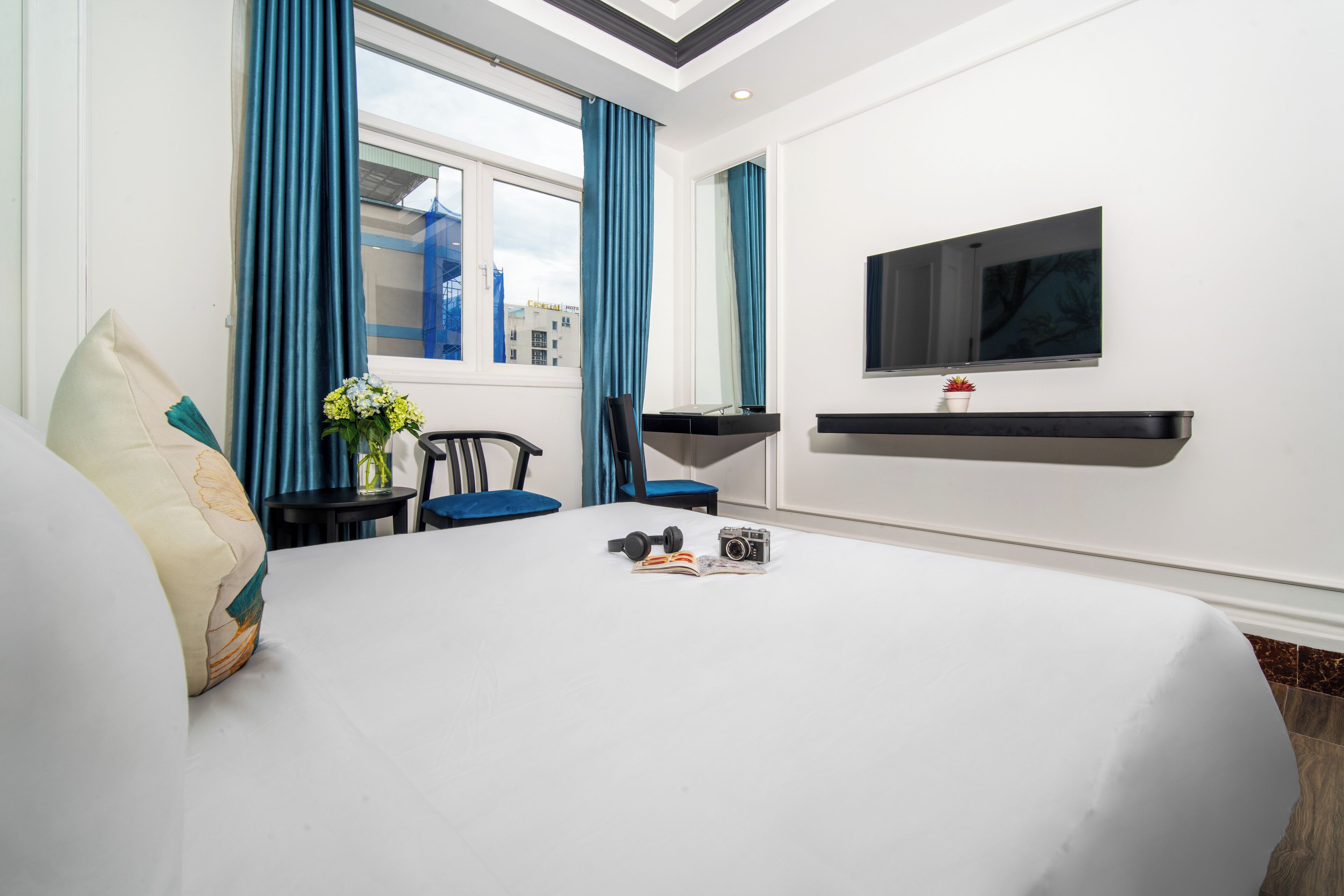 Habitación de hotel con cama, escritorio con silla, televisor montado en la pared y ventana con cortinas.
