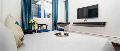 Habitación de hotel con cama, escritorio con silla, televisor montado en la pared y ventana con cortinas.