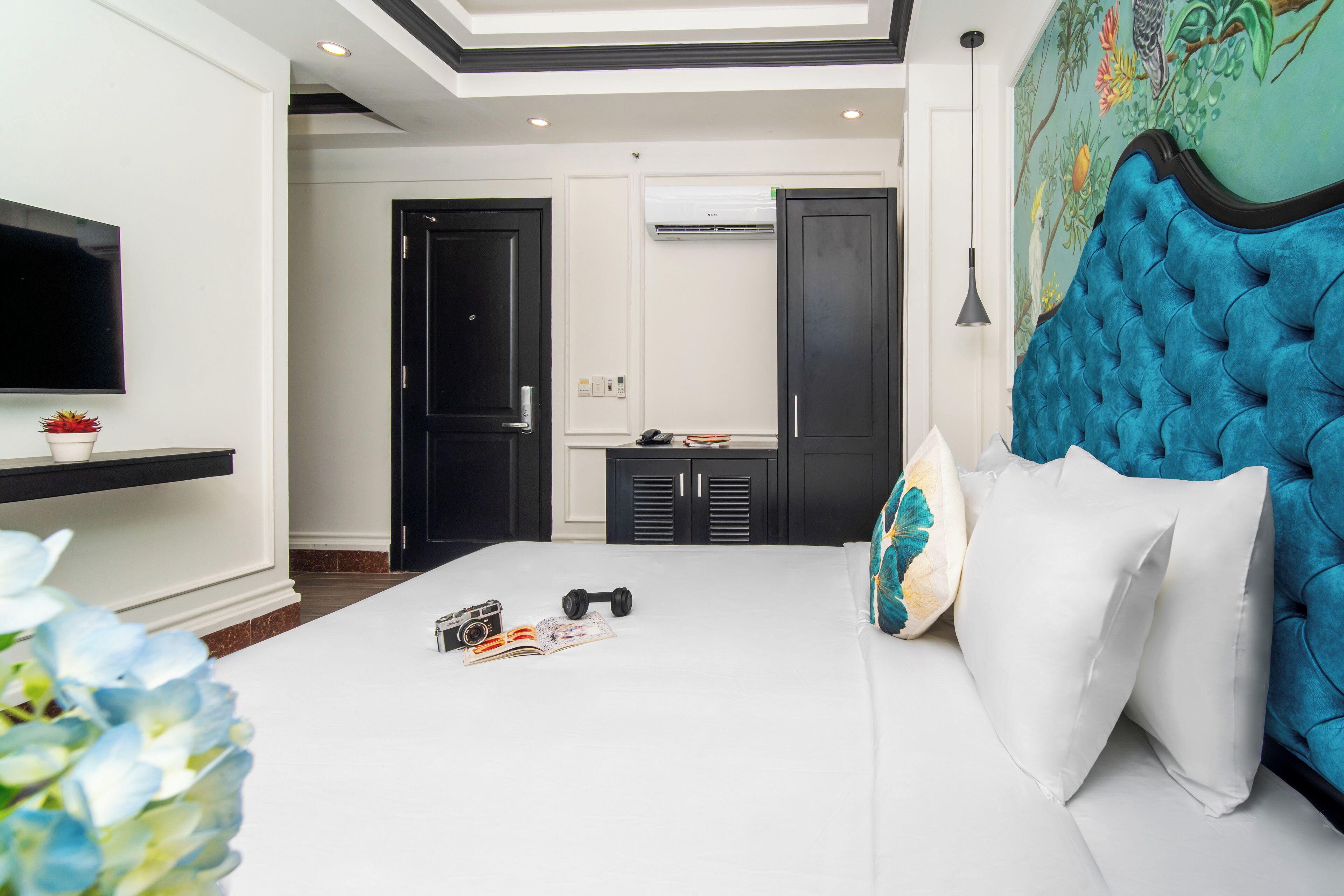 A modern hotel room with a large bed, a flat-screen TV, a wall-mounted air conditioner, and a decorative mural.