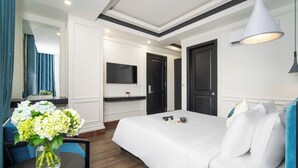 Ett hotellrum med en säng, ett skrivbord med en stol, en tv som är monterad på väggen och en vas med blommor på skrivbordet.