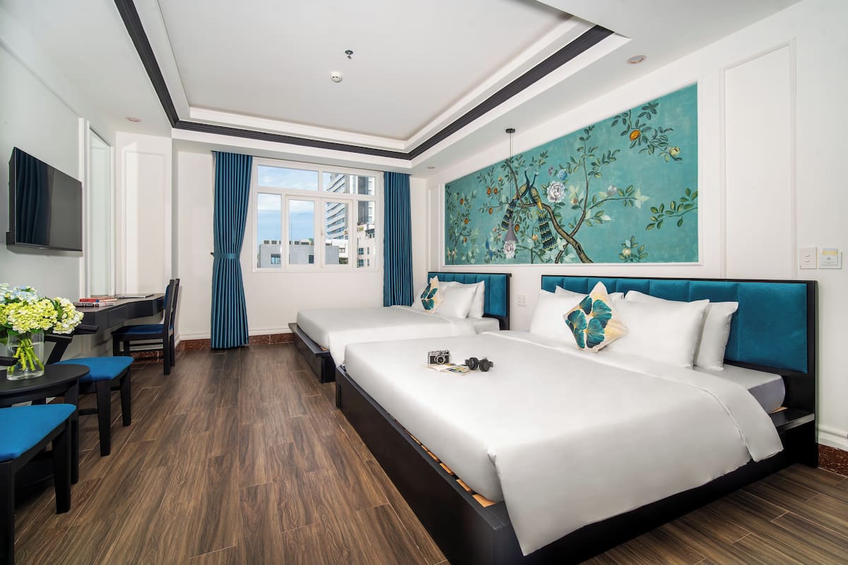 Habitación de hotel con dos camas, un escritorio con silla, televisor y un ventanal con cortinas.