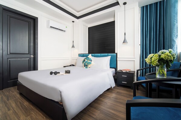 Una habitación de hotel moderna con una cama grande, una mesita de noche, un escritorio con silla y una ventana con cortinas.