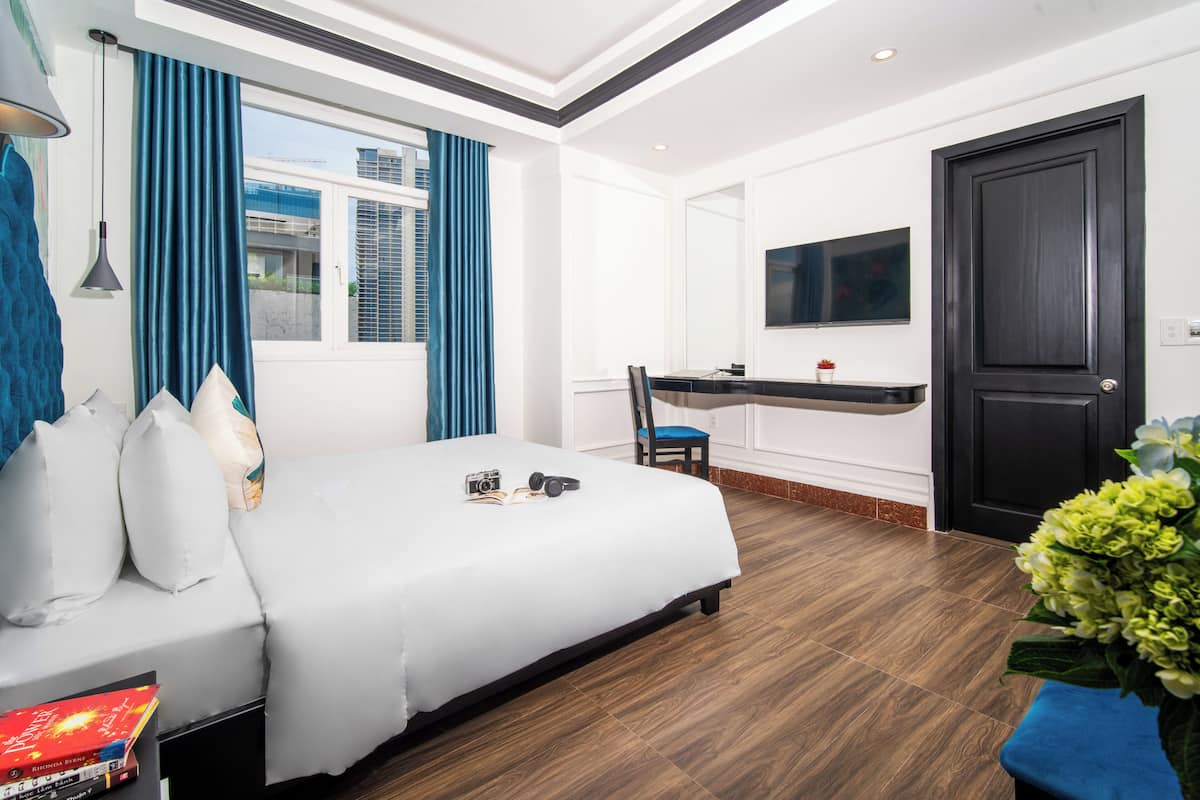Habitación de hotel con cama, escritorio, silla, televisor y ventana con cortinas.