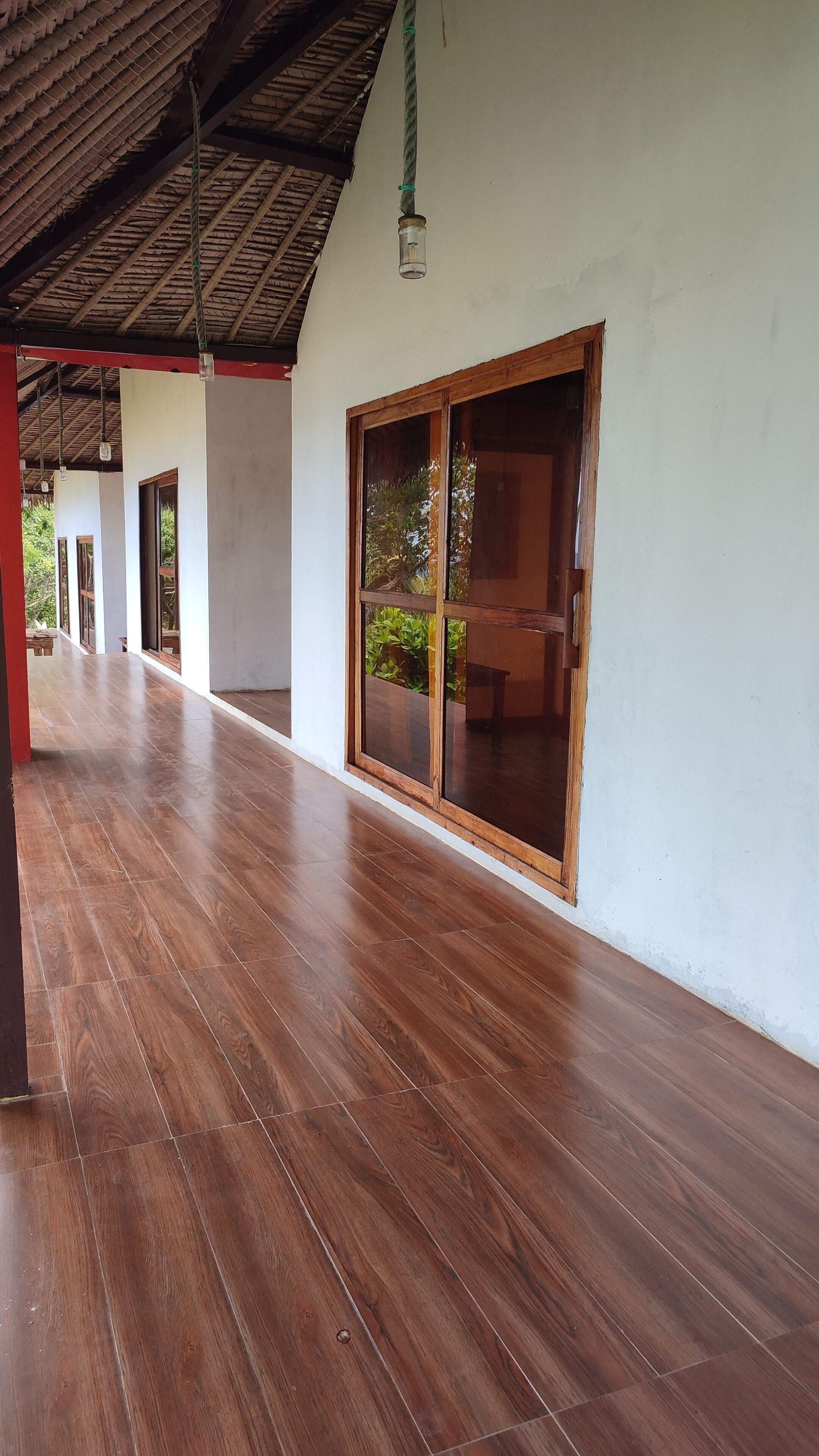 Una terraza cubierta de madera con grandes puertas correderas de vidrio y un techo de paja.