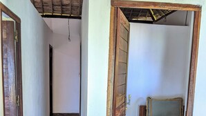 A narrow hallway with a tiled floor leading to a room with a bed and a wooden door.