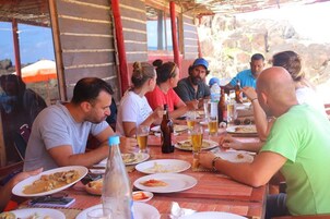 Un grupo de personas cenando en una mesa de madera al aire libre, con bebidas y platos de comida.