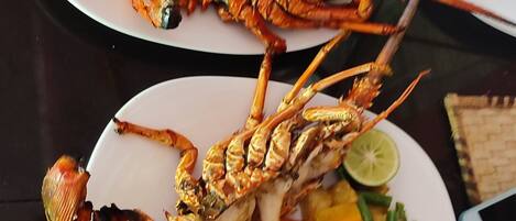 A dining table with plates of grilled lobster and mixed vegetables.