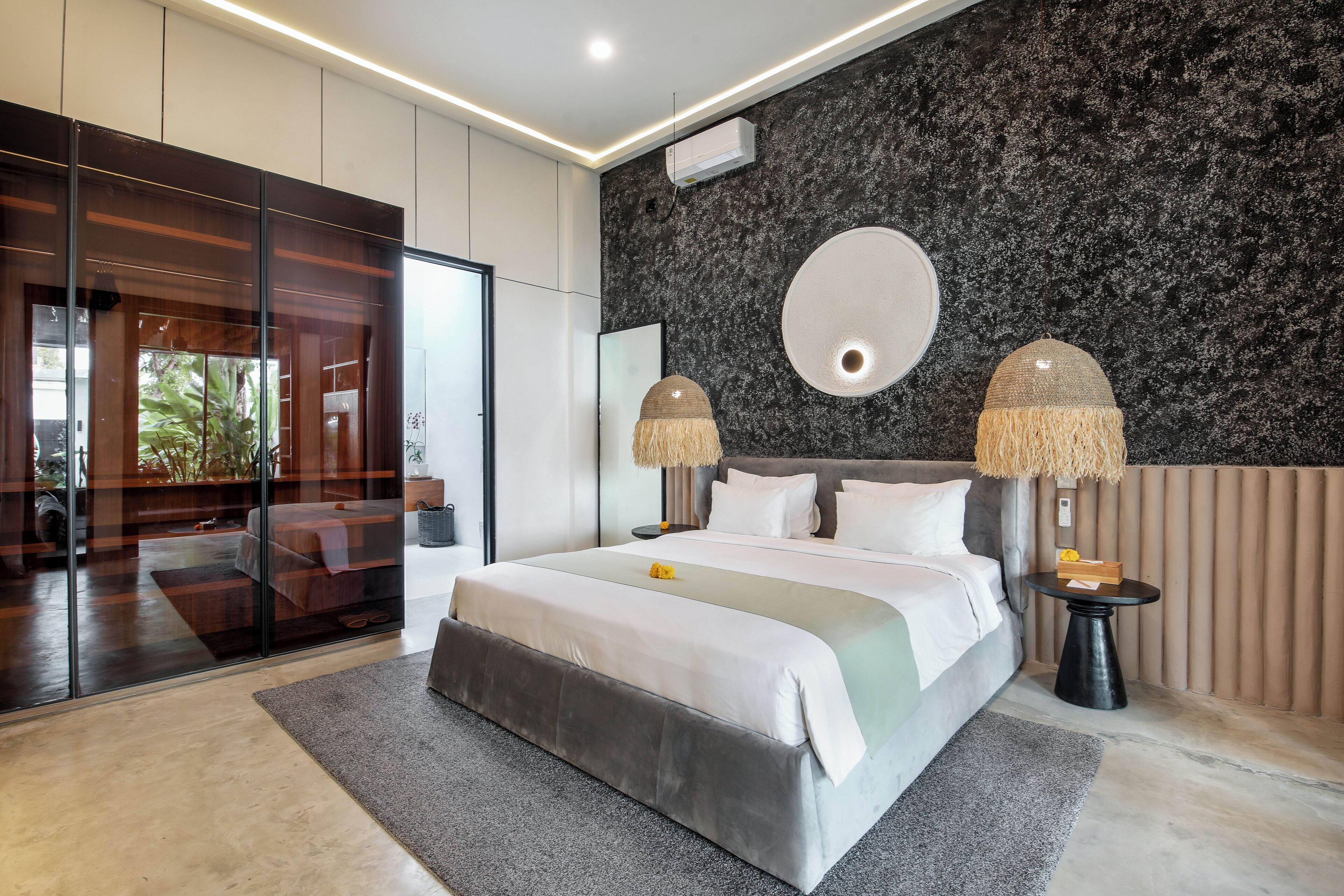 A modern bedroom with a large bed, a glass door leading to a balcony, a round mirror, and two lamps.