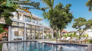 Ein modernes Haus mit Swimmingpool, Glasüren und einem Garten mit Liegestühlen.
