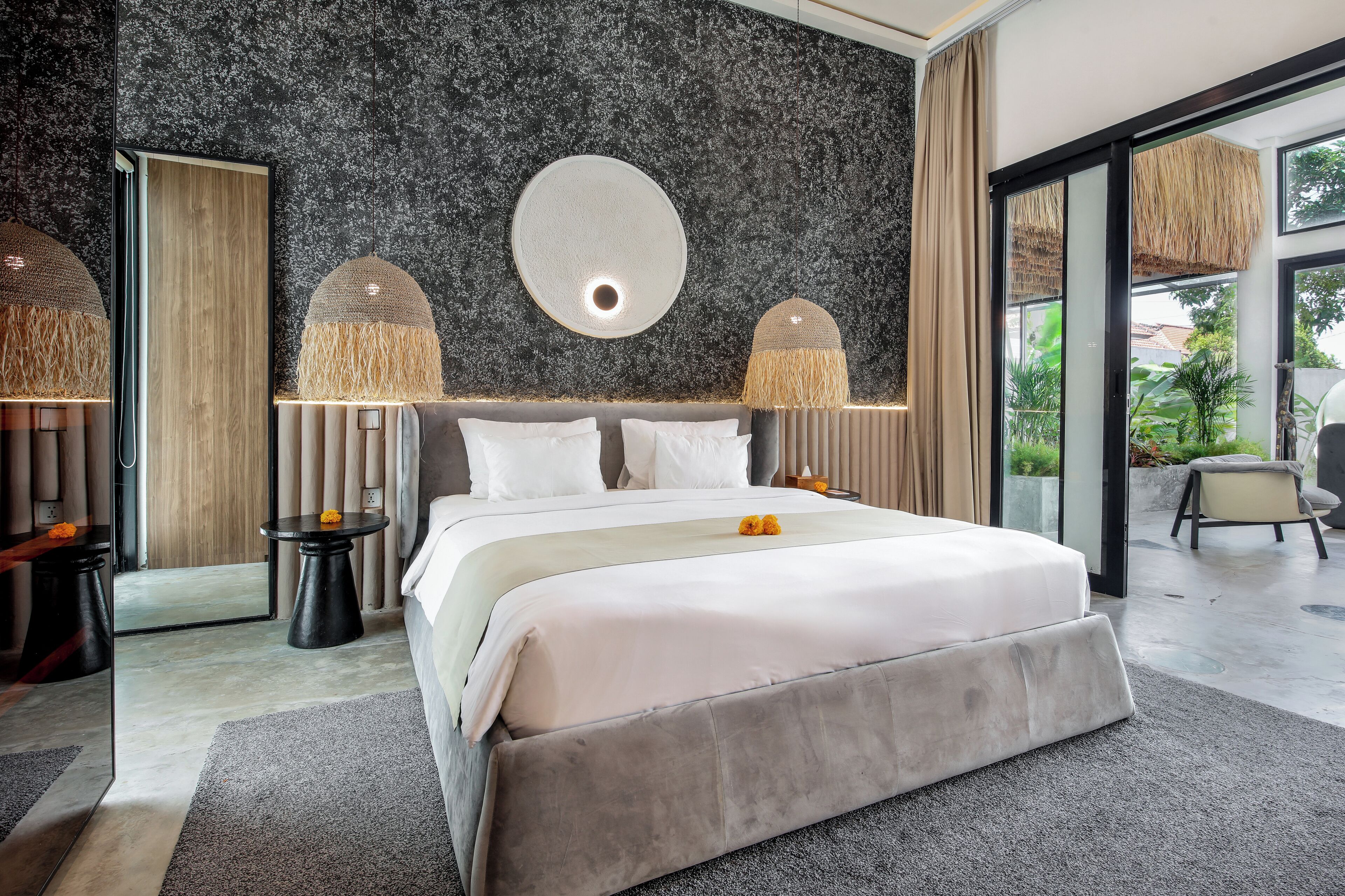 Un dormitorio moderno con una cama grande, dos mesitas de noche, un espejo redondo y vistas al exterior.